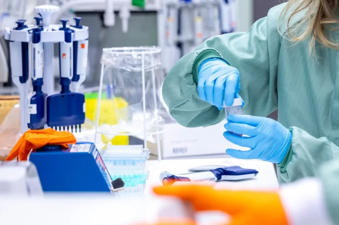 Handsbeklädda händer som skruvar på ett lock inne på ett labb