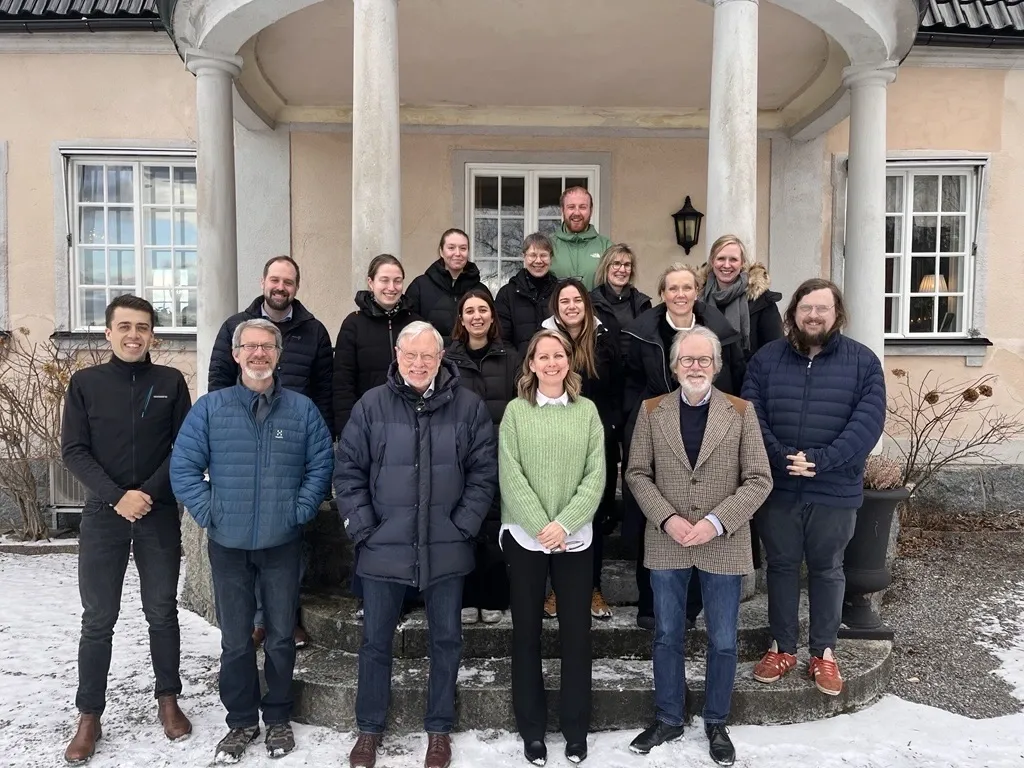 Group photo of about fifteen people standing on a staircase in front of the entrance to a house.