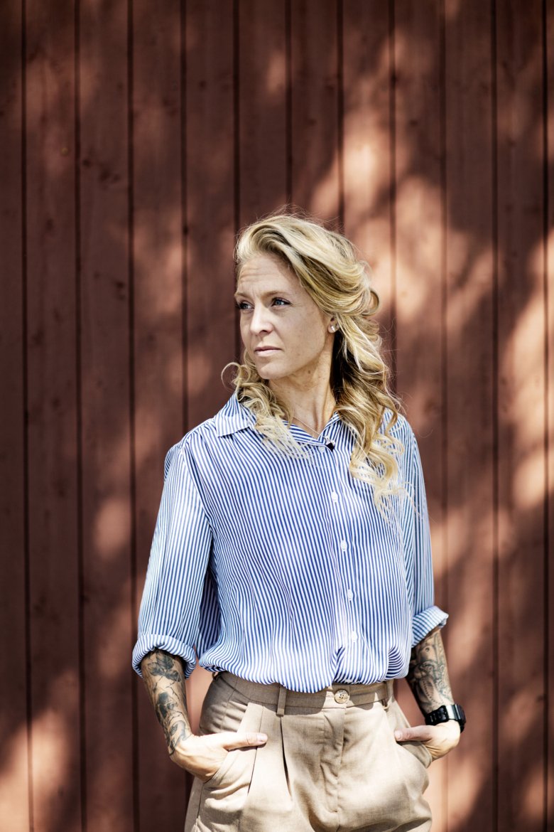 Portrait of Elin Mohlin standing against wooden wall outside.