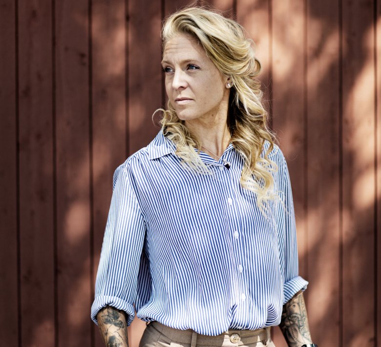 porträttbild av Elin Mohlin som står framför falurött trävägg ute.