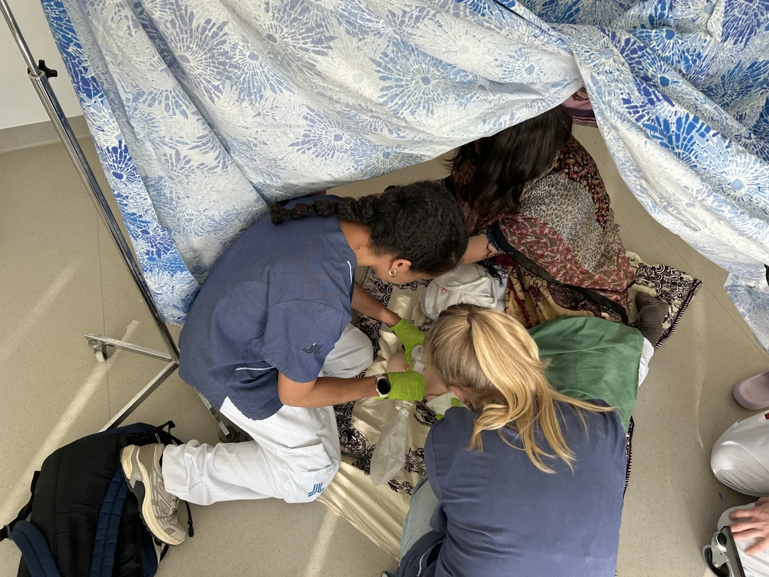Three people sitting on the floor in a makeshift tent practicing on a doll