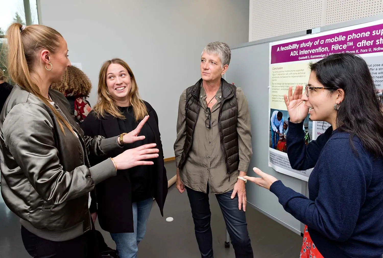 3 arbetsterapeutstudenter och 2 lärare står vid en poster och diskuterar