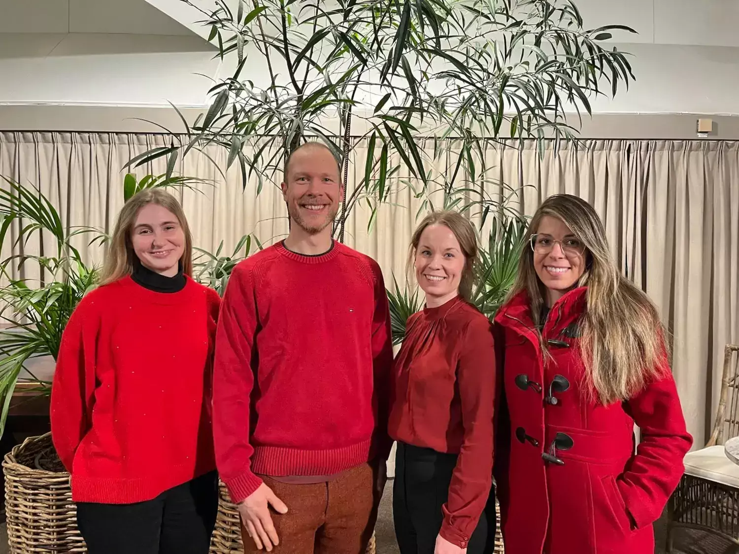 Four people wearing red tops, looking at the camera and smiling.