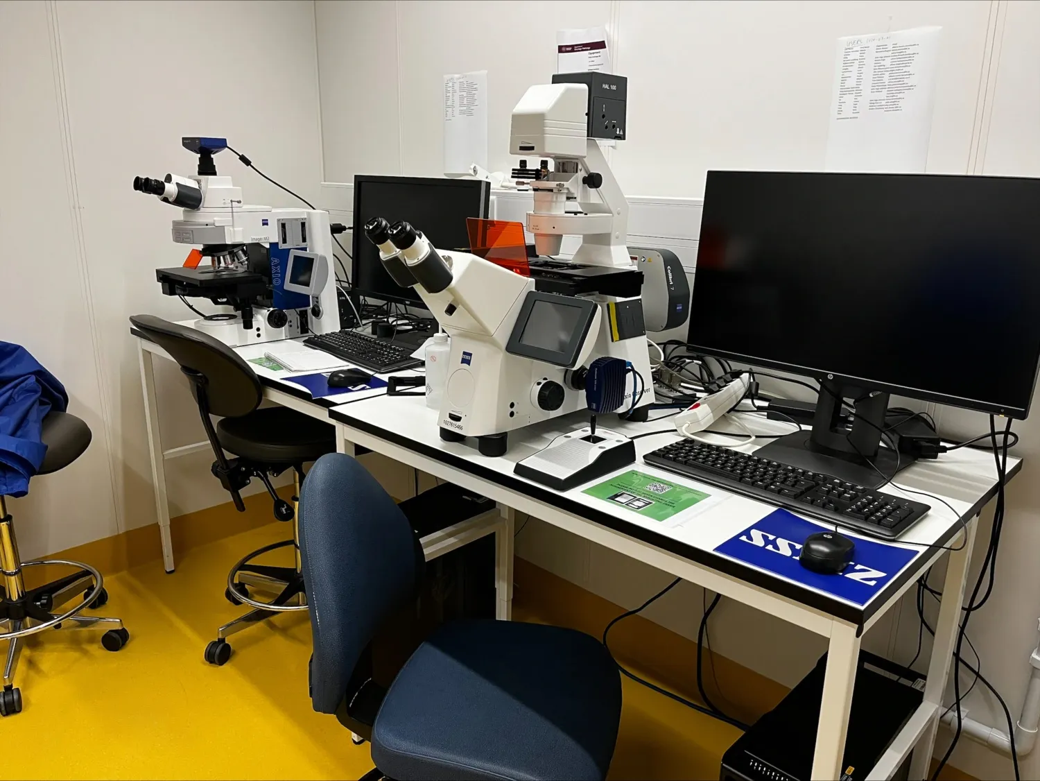 Two microscopes and computer screens on a desk.