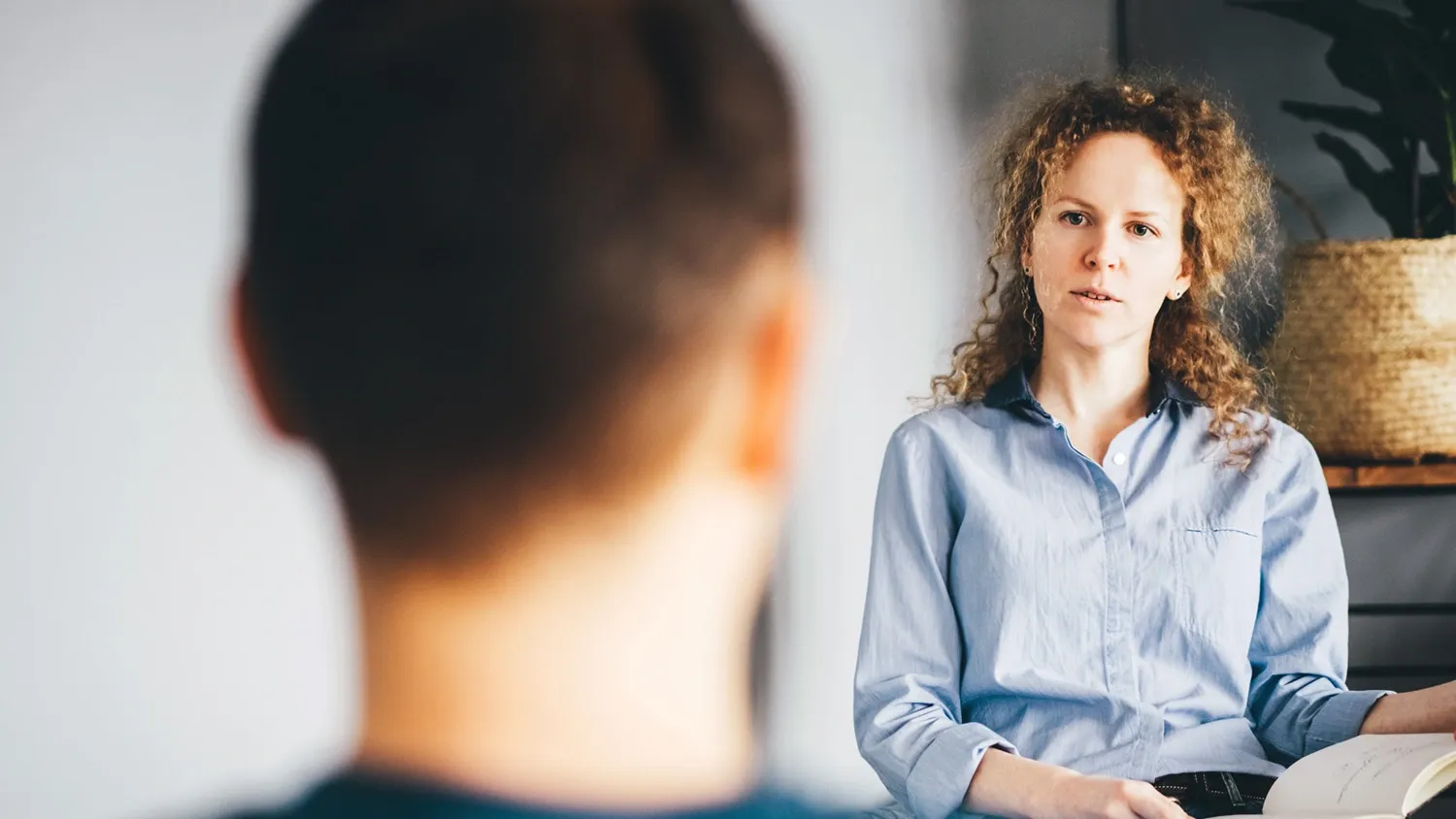 A woman in a light coloured shirt in front view. The back of a man's head blurred in the foreground.