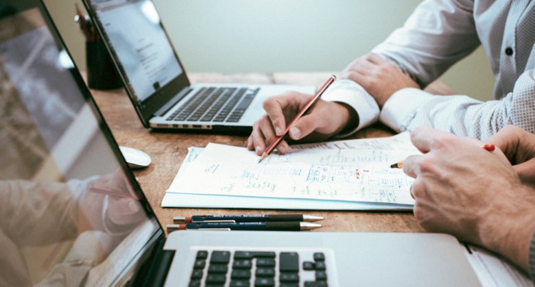 Bilden visar två personer som tittar på två datorskärmar och skriver anteckningar vid sidan om.