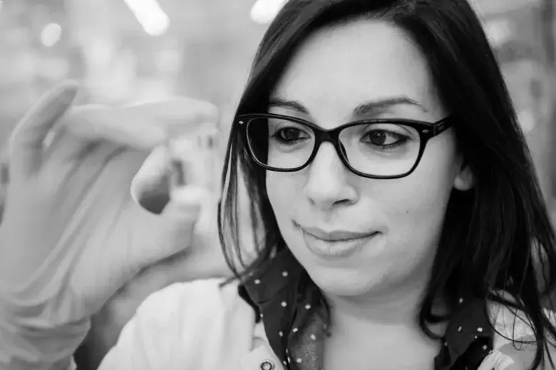 Scientist wearing rubber gloves, holding up a small glass container.