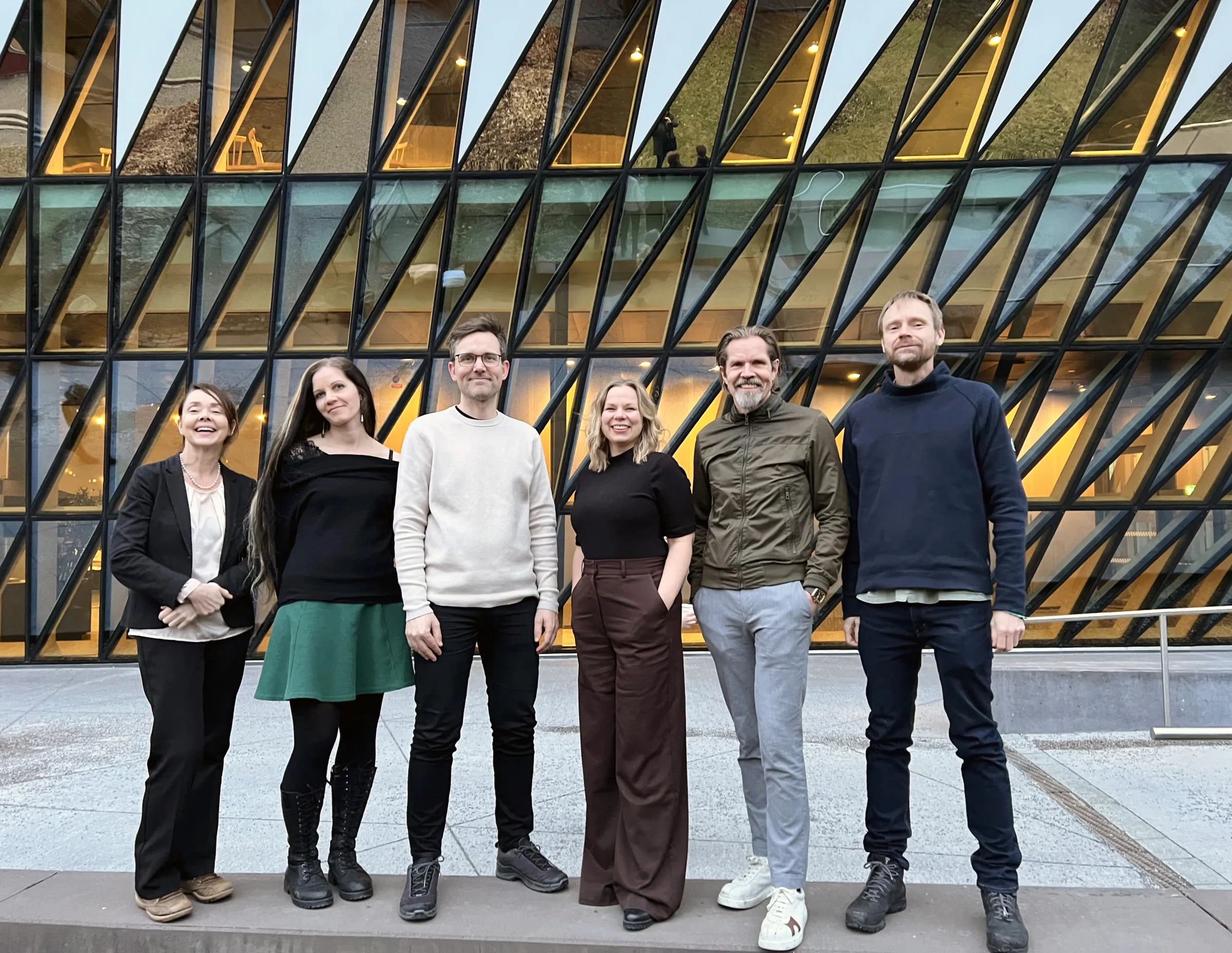 Bild på tre kvinnor och tre män som står på rad framför en glasfasad.