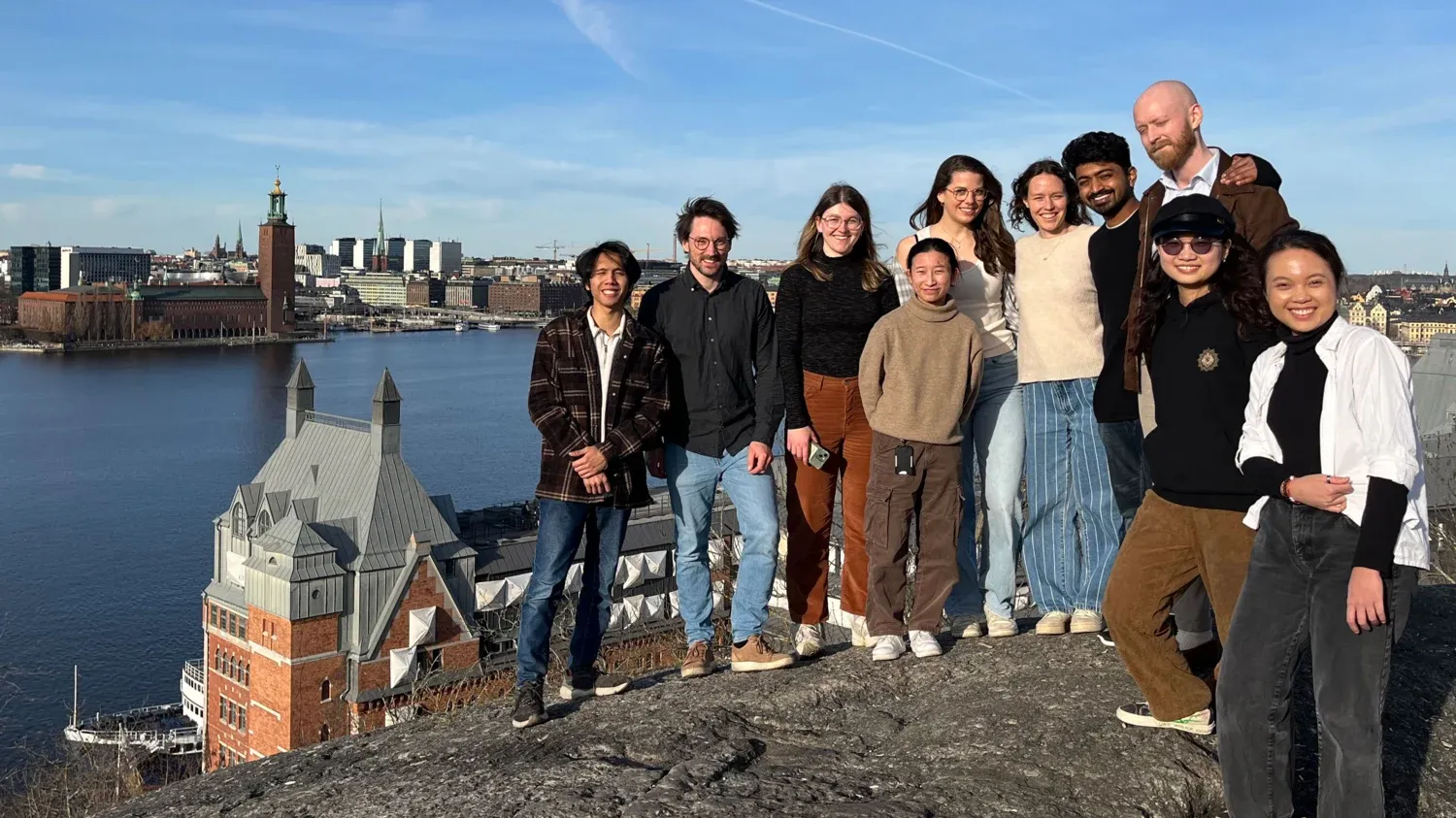 A group photo of 10 people standing on a cliff with a view of Stockholm in the background.