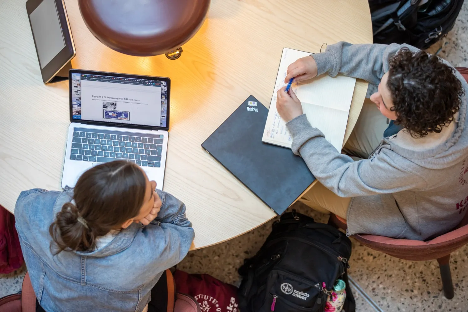 Students indoors at campus Solna during the spring semester of 2022. || Students hanging out indoors on campus. || Two students sitting at a table having a conversation