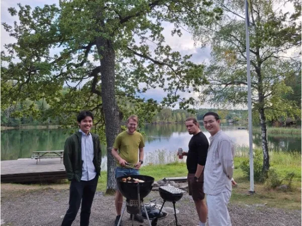 Four men standing around a BBQ, cooking and socialising.