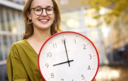 Researcher Theresa Lemke holding a clock displaying 9 am.